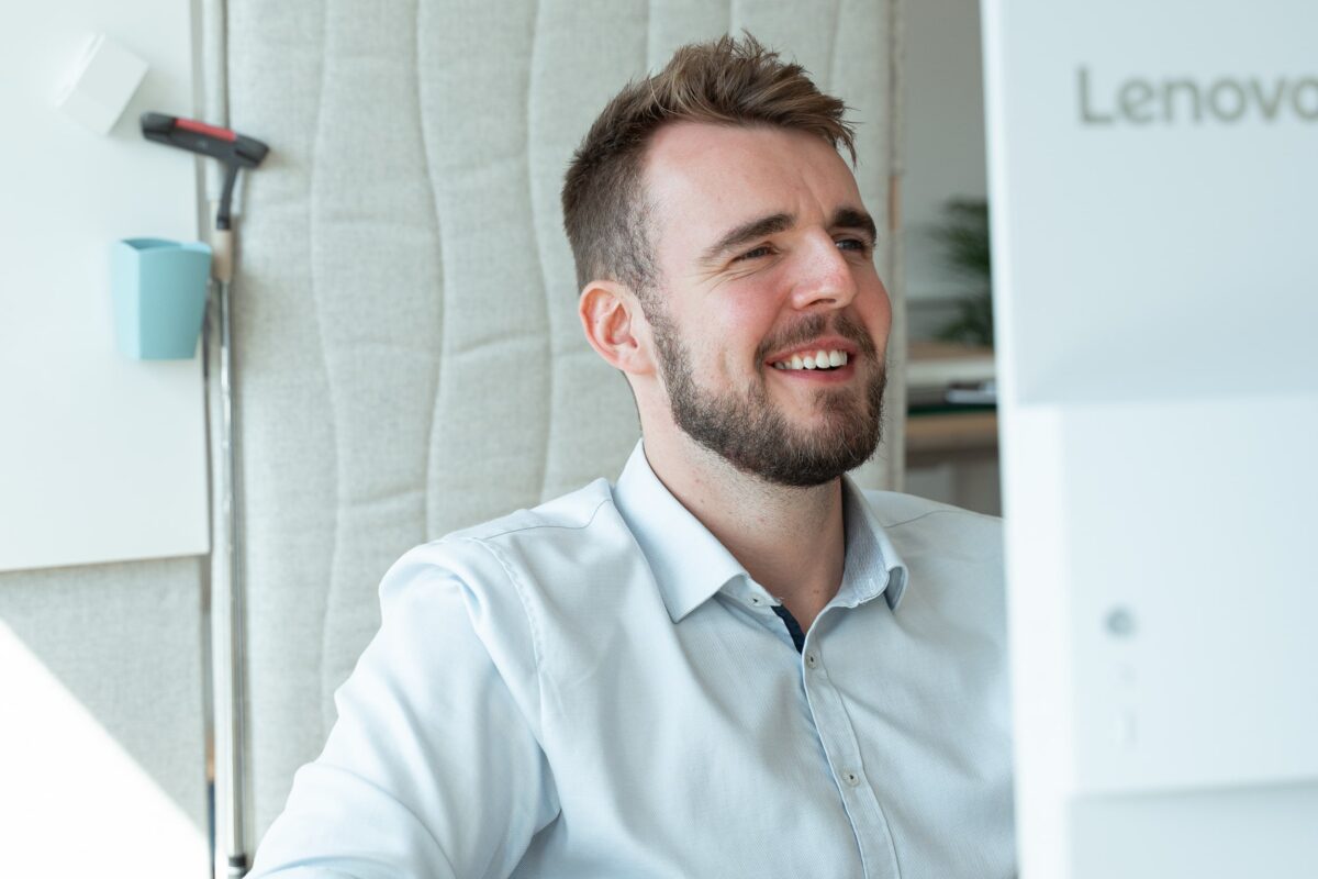 Man smiling at computer in bright office setting.