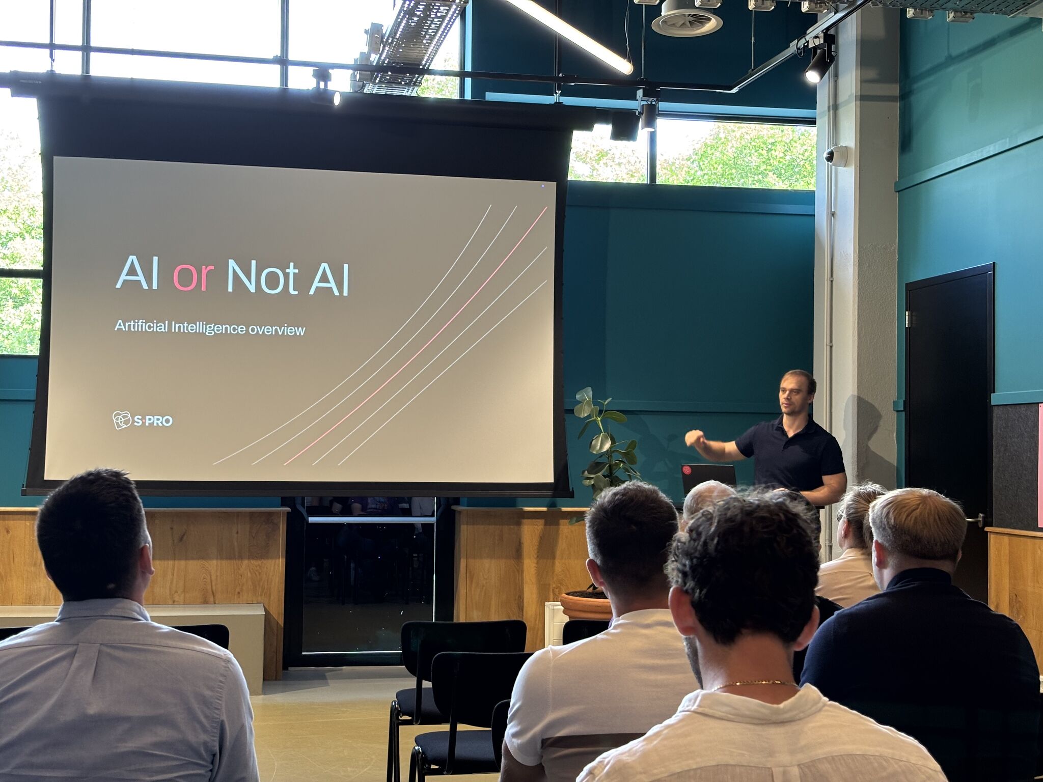 Man presenting AI or Not AI slide to an audience in a modern, well-lit conference room.