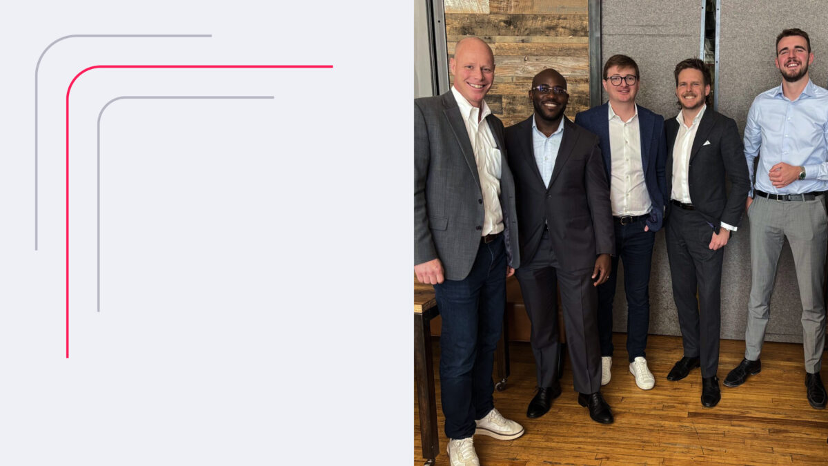 Business team smiling at a professional gathering. Five men in formal attire standing indoors.