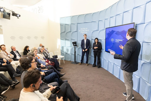 People attending a presentation at the World Economic Forum 2023, with speakers at the front and a large screen.