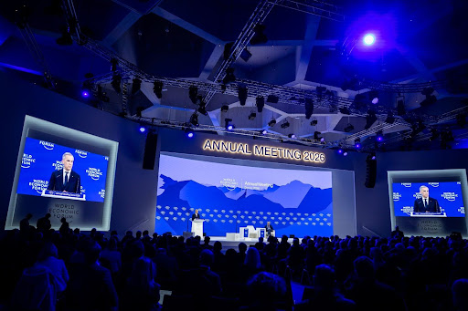 Speaker addressing a large audience at the Annual Meeting 2026, with blue-themed stage and screens displaying the event name.
