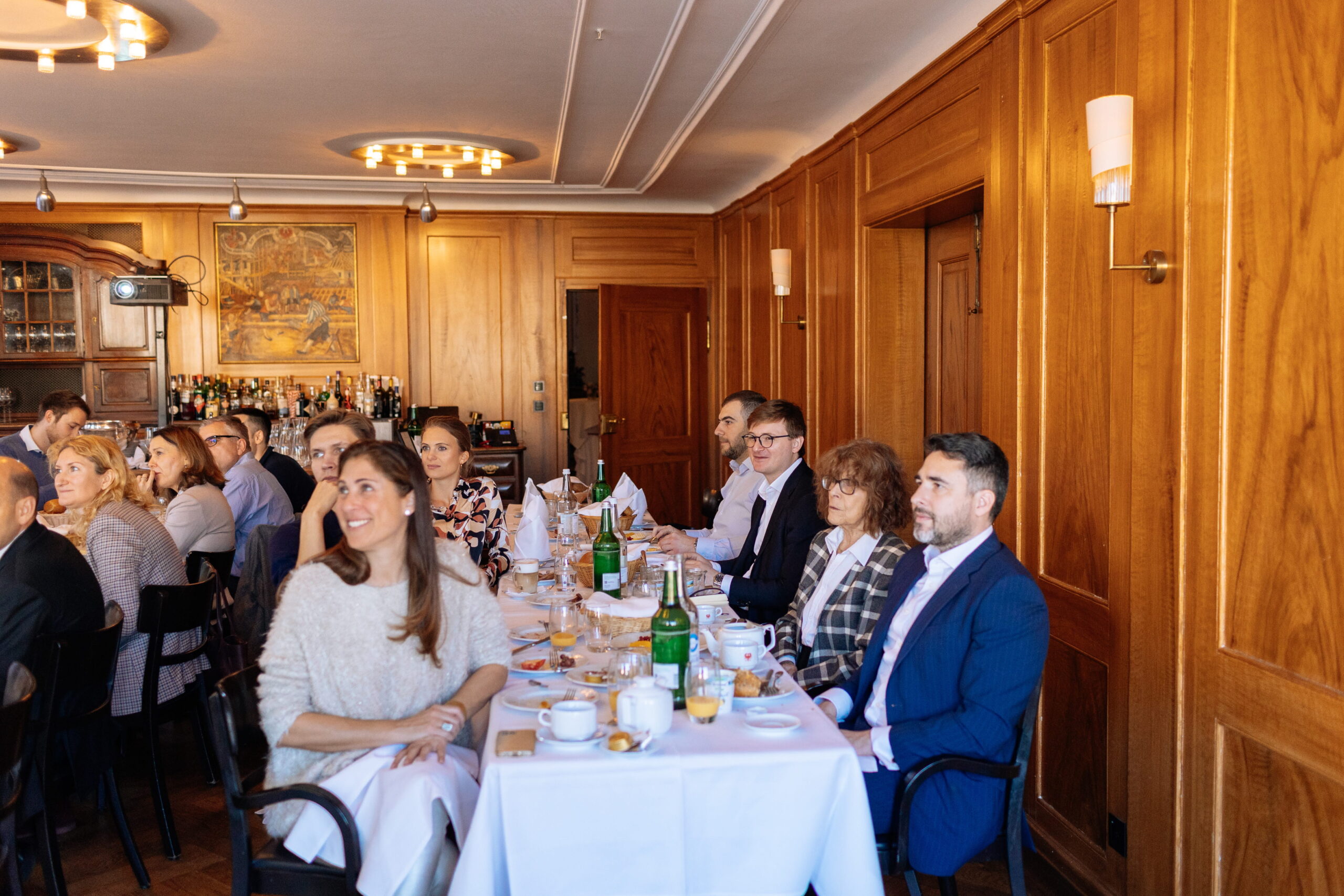 Business meeting in a wood-paneled room with engaged attendees seated at a long table.