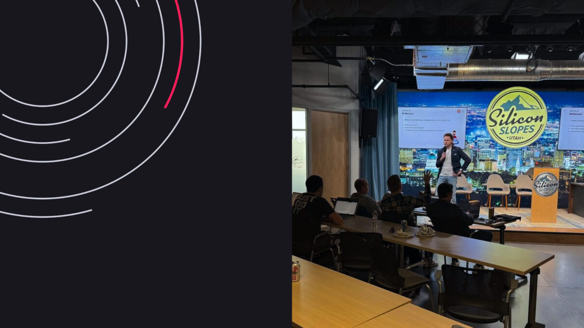 Presentation at Silicon Slopes event with speaker on stage, audience seated, and city backdrop.