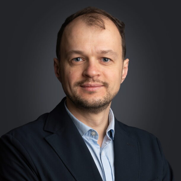 Professional portrait of a man in a dark suit, light blue shirt, with a neutral background.