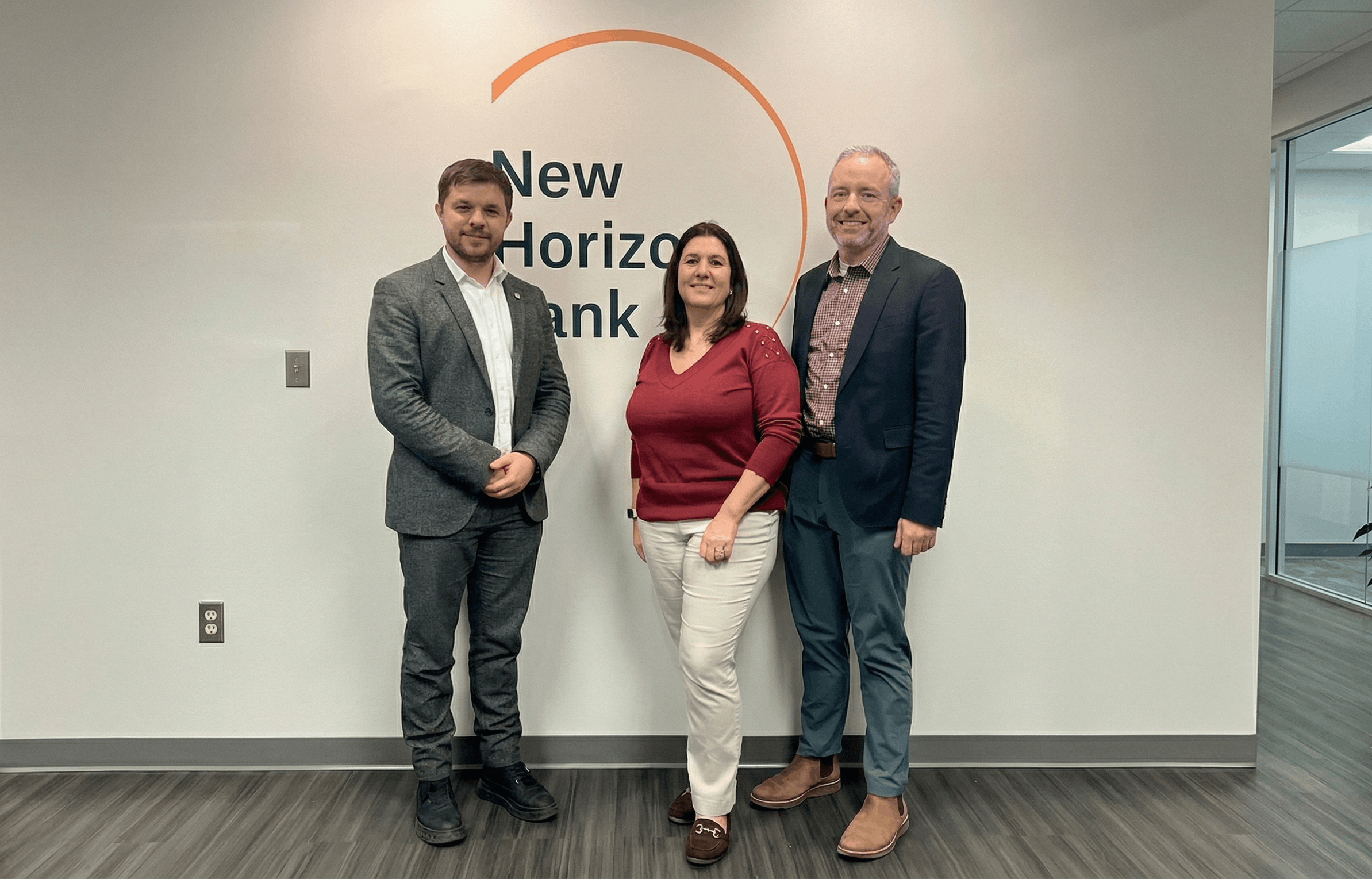 Three people smiling in front of New Horizon Bank sign in an office setting.