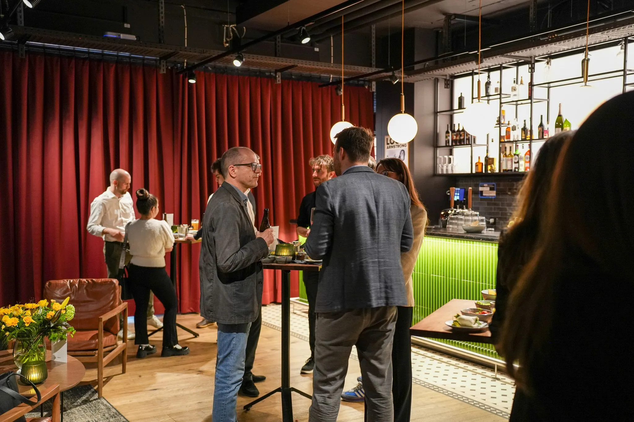 People networking at a stylish modern bar with red curtains and hanging lights.