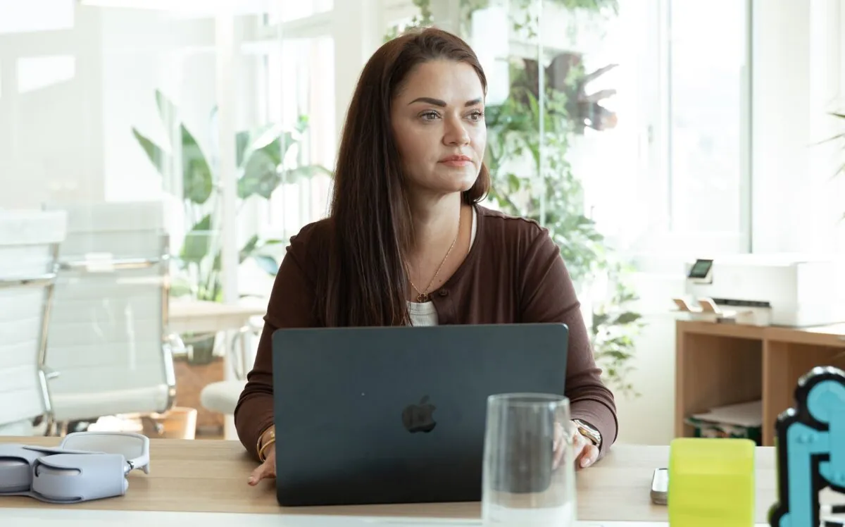 Woman working on laptop in a bright office with plants in the background.