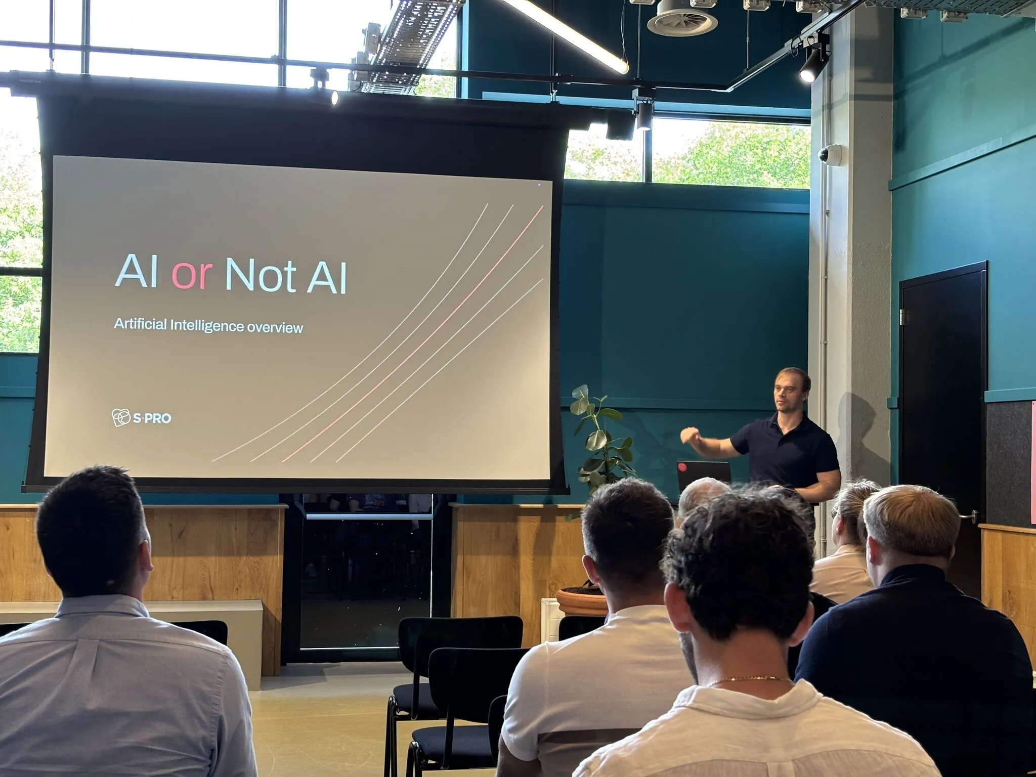 Man presenting AI or Not AI slide to an audience in a modern, well-lit conference room.