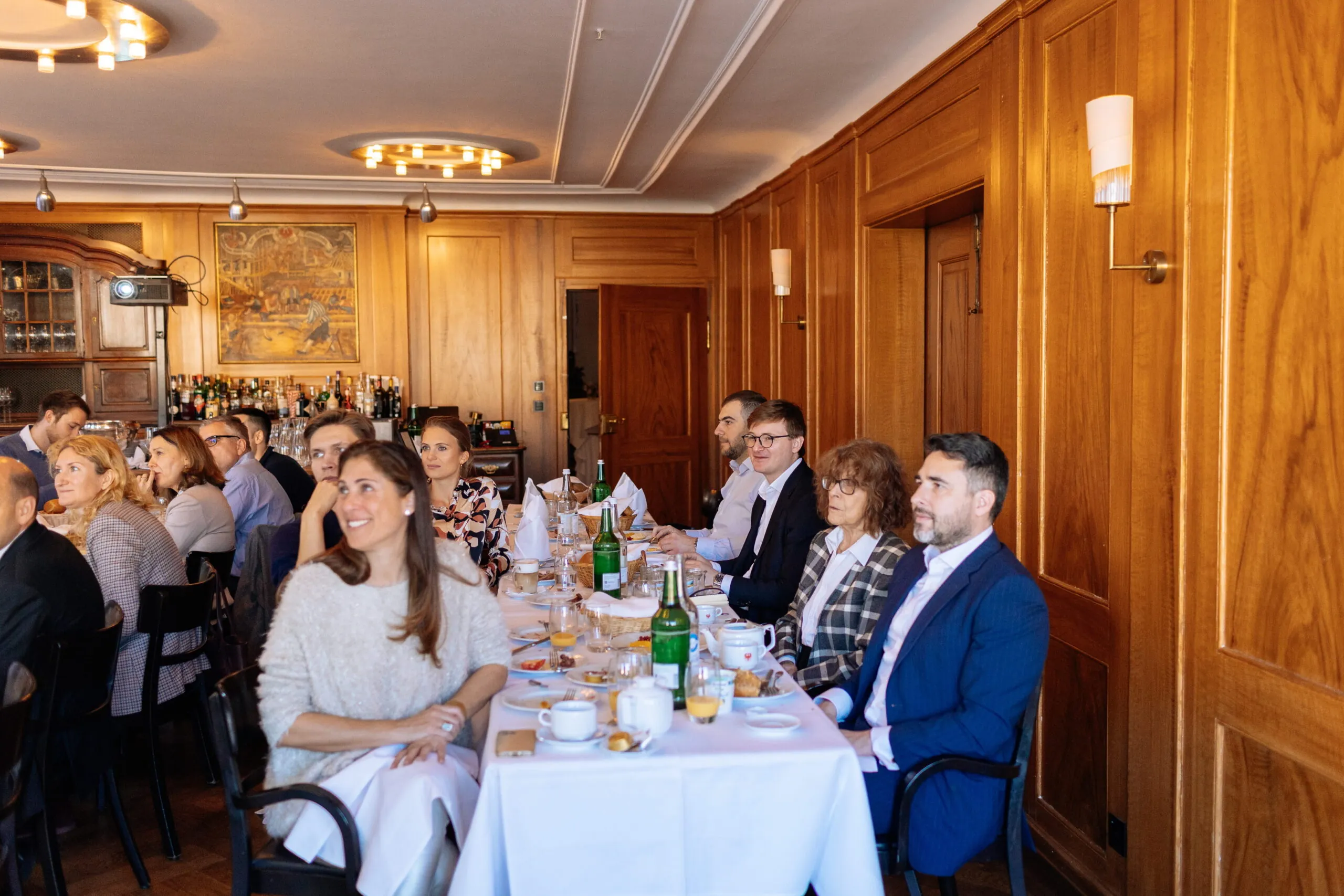 Business meeting in a wood-paneled room with engaged attendees seated at a long table.