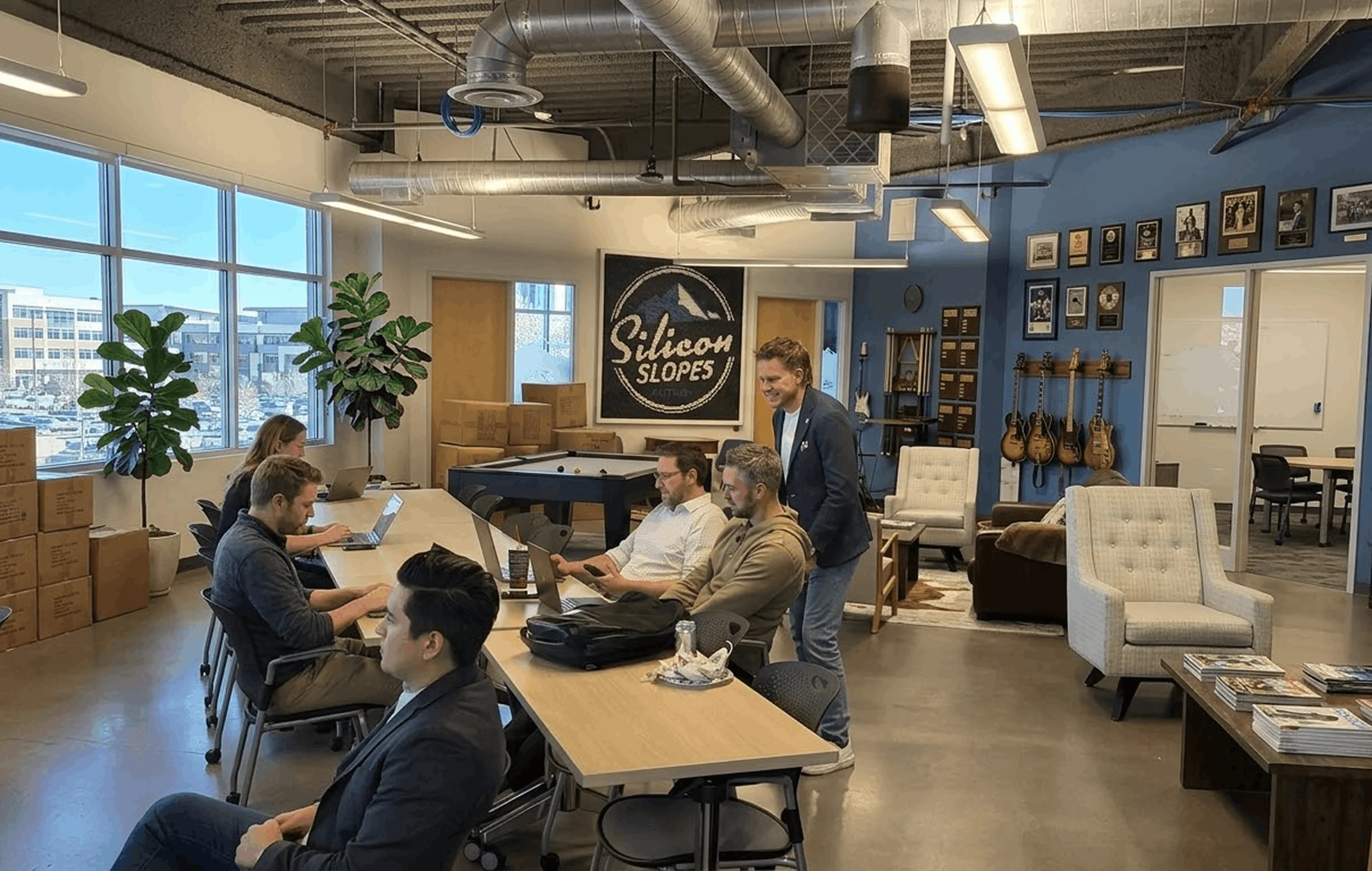 Office team collaborating on laptops in a modern workspace with Silicon Slopes sign and instruments displayed.