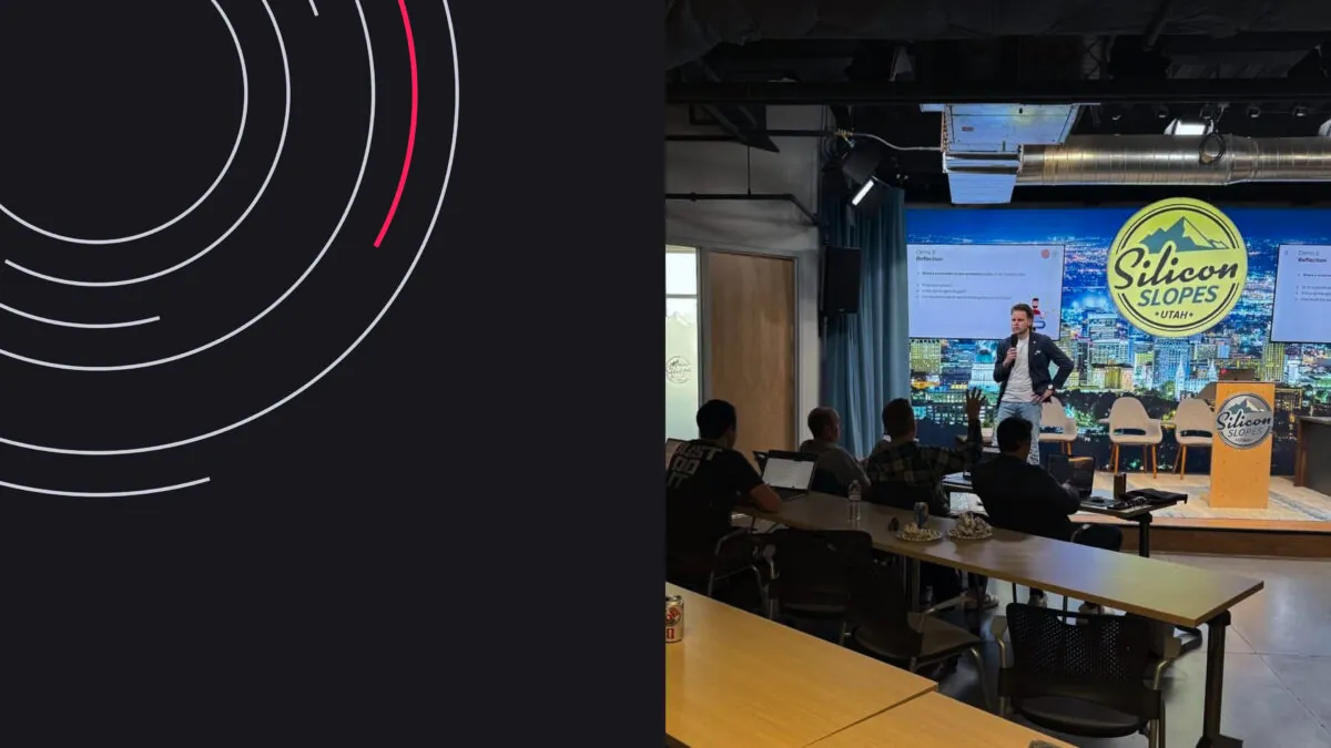 Presentation at Silicon Slopes event with speaker on stage, audience seated, and city backdrop.