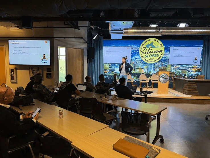 Speaker presenting at Silicon Slopes Utah conference with audience in attendance, large logo displayed on stage.